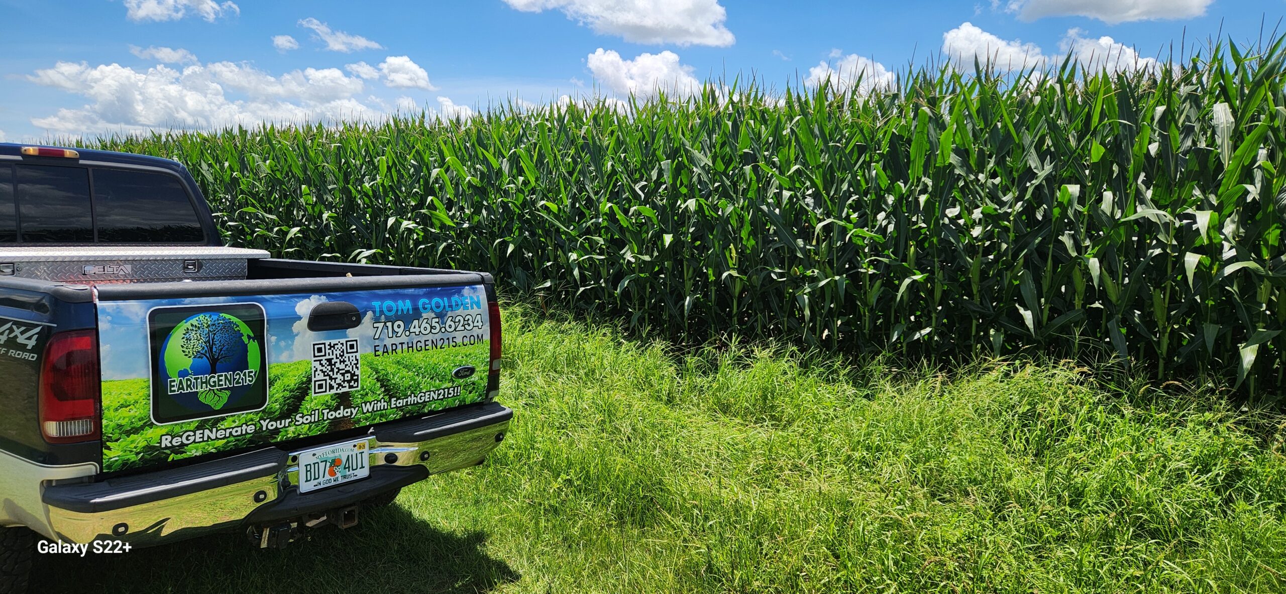 A pickup truck with "EarthGen 215" branding parked beside a lush cornfield under a blue sky, promoting soil regeneration services.